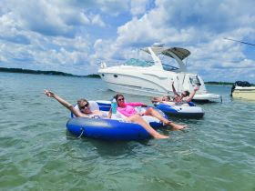 A fun group enjoys a sunny day on the water, relaxing on inflatable tubes while a boat is anchored nearby — perfect for summer parties and water activities.