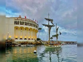 A picturesque sailboat docked at a harbor, with a stunning backdrop of a historic building and palm trees, perfect for capturing the essence of coastal adventures.