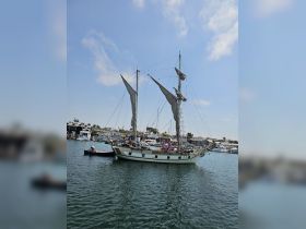 A beautiful sailboat docked in the harbor with people visible on board, showcasing a vibrant maritime atmosphere perfect for sailing adventures.