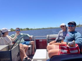 A lively group enjoys a sunny day on a pontoon boat, sharing drinks and laughter on the water — perfect for a fun outing with friends.