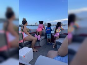 A family enjoys a scenic boat ride, with children captivated by the view of the water and skyline — a perfect moment for summer adventures.