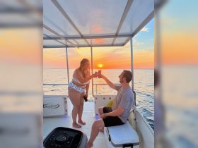 A couple toasts cocktails on a boat at sunset, creating a romantic atmosphere perfect for special celebrations on the water.