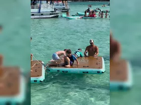 A lively scene of kids playing on floating platforms in clear turquoise waters, showcasing the joy of summer water activities and family fun.
