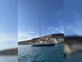 A stunning sailboat anchored near rocky cliffs, showcasing the beauty of the coastline and clear blue waters — perfect for sailing adventures.