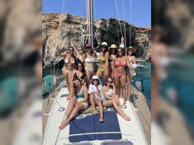 A lively group of friends poses on the deck of a sailboat, enjoying a sunny day at sea — perfect for bachelorette parties or group celebrations.