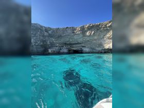 A stunning view of a rocky coastline with a cave entrance, surrounded by crystal-clear turquoise waters — a perfect destination for exploration and adventure.