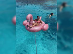 A woman enjoys a sunny day floating on a pink flamingo inflatable in crystal-clear waters, while a friend snorkels nearby — a perfect scene for summer fun and relaxation.