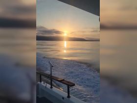 A serene sunset view from the deck of a boat, showcasing the tranquil waters and distant mountains — perfect for peaceful evening cruises.
