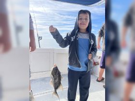 A young boy proudly holds up his catch while fishing on a boat, showcasing the excitement of a successful fishing trip.