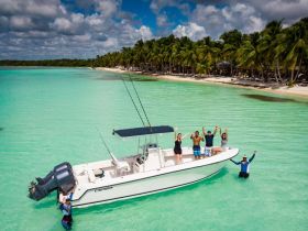 A lively group celebrates aboard a boat in stunning turquoise waters, surrounded by a picturesque beach — perfect for unforgettable adventures on the water.