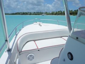 A bright and inviting interior view of a boat's helm and seating area, showcasing comfortable white cushions against a backdrop of stunning turquoise waters.