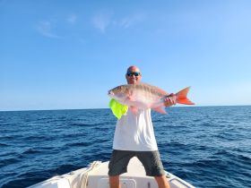 A proud angler holds up a large fish while standing on a boat in the open ocean, showcasing the thrill of a successful fishing trip.