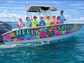 A group of children and an adult enjoy a fishing trip aboard the vibrant 'Reely Salty' boat, showcasing a fun day on the water filled with adventure and camaraderie.