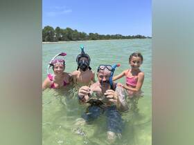 A family enjoys a fun snorkeling adventure, proudly displaying a crab caught in the shallow waters — a memorable wildlife encounter perfect for summer outings.