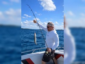 A man proudly displays his catch while fishing on a boat, showcasing the thrill of a successful day on the water.