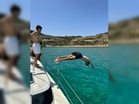 A group of friends enjoys a thrilling moment as one dives off the side of a boat into the crystal-clear waters, capturing the essence of summer fun and adventure on the water.