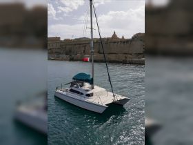 A stunning catamaran docked in calm waters, showcasing its sleek design against a historic backdrop — perfect for leisurely sailing adventures.