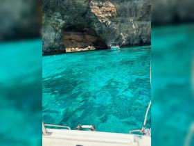 A stunning view of a cave entrance surrounded by crystal-clear turquoise waters, with a boat nearby and swimmers enjoying the beautiful scenery.