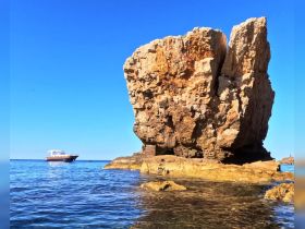 A picturesque view of a rocky coastline with a boat anchored nearby, showcasing the natural beauty of the area — perfect for scenic boat tours and exploration.