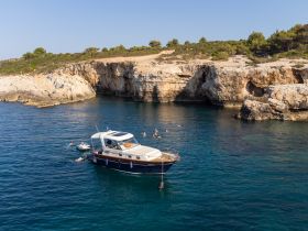 A lively scene of swimmers enjoying the clear waters near a boat, set against a stunning rocky coastline — perfect for summer adventures and coastal exploration.