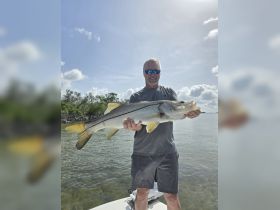 A proud angler holds up a large snook caught while fishing from a boat, showcasing the thrill of a successful day on the water.