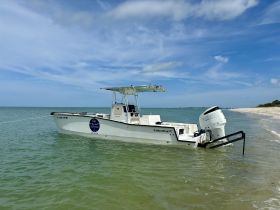 A center console boat named CalcuttaX is docked in calm waters, showcasing its sleek design against a backdrop of clear skies and sandy shores.