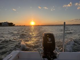 A stunning sunset view from the back of a boat, showcasing the engine and the shimmering water as the vessel moves through the scenic landscape.