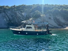 Two individuals enjoy a sunny day aboard a boat near a stunning coastline, showcasing the perfect setting for a summer adventure on the water.