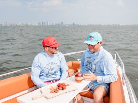 Two friends enjoy cocktails and a delicious spread aboard a boat, perfect for a relaxing day on the water with great company.
