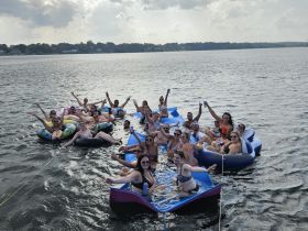 A lively group enjoys a fun day on the water, floating on colorful inflatables and celebrating together — perfect for summer gatherings and parties.