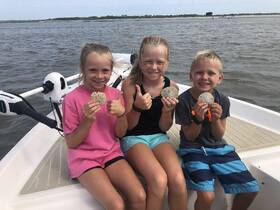 Three children proudly display their sand dollars while enjoying a fun day on the boat — a perfect family adventure on the water.