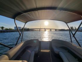 A serene view from the interior of a boat, showcasing comfortable seating and a picturesque sunset reflecting on the water — perfect for relaxing cruises.