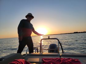 A man enjoys a stunning sunset on the water, showcasing the serene beauty of a boating experience.