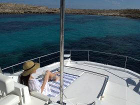 A woman relaxes on the deck of a yacht, enjoying a drink while taking in the stunning turquoise waters — a perfect moment for leisure and tranquility on the water.