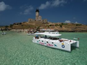 A lively scene at a picturesque island with a catamaran anchored nearby, as groups of people explore the beach and enjoy the clear waters — perfect for a day of adventure and relaxation.