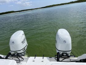 Close-up view of two Suzuki outboard motors mounted on a boat, showcasing the vessel's engine setup against a serene water backdrop.