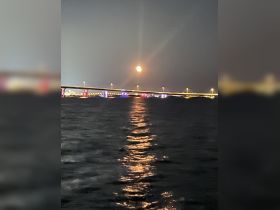 A stunning view of the moon reflecting on the water, with a beautifully lit bridge in the background — perfect for capturing serene nighttime moments on the water.