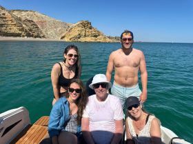 A cheerful group of friends enjoys a sunny day on the water, capturing memories aboard their boat against a stunning coastal backdrop.