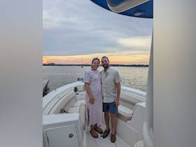 A couple poses for a photo on their boat at sunset, capturing a perfect moment of joy and togetherness on the water.