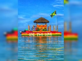 A vibrant tiki boat named 'One Two Love' anchored in calm waters, showcasing the colorful design and Jamaican flag — perfect for tropical adventures.