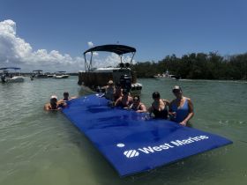 A lively group enjoys a fun day on a floating mat in the water, surrounded by boats — perfect for summer parties and relaxation on the water.