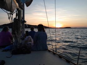 A group of friends enjoys a stunning sunset from the deck of a sailboat, creating a perfect backdrop for memorable moments on the water.
