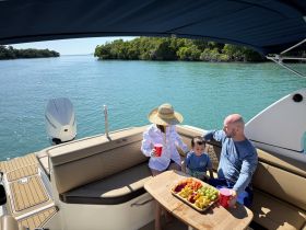 A family enjoys a relaxing day on the water, sharing a colorful platter of snacks aboard their boat, surrounded by serene views of nature.