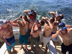 A lively group of friends enjoys a fun fishing trip, celebrating with drinks on the deck of a boat — perfect for summer adventures on the water.