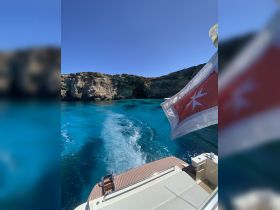 A stunning view from the back of a boat cruising through crystal-clear turquoise waters, showcasing the beautiful cliffs and vibrant marine environment.