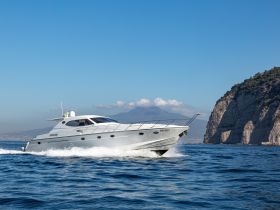 A sleek yacht cruises through clear waters, showcasing its elegant design against a stunning coastal backdrop — perfect for luxury boating experiences.
