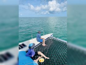 Two guests relax on the deck of a boat, enjoying snacks while taking in the serene ocean view — a perfect moment for unwinding on the water.