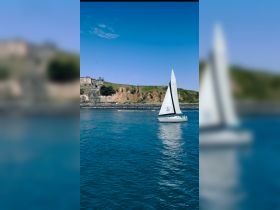 A beautiful sailboat glides through calm waters, showcasing its elegant design against a scenic coastal backdrop.