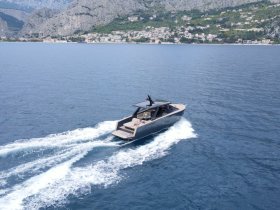 A sleek speedboat glides through the clear blue waters, showcasing its modern design against a stunning coastal backdrop.