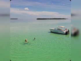 Two individuals enjoy swimming in the crystal-clear waters while a boat is anchored nearby, creating a perfect scene for a fun day on the water.